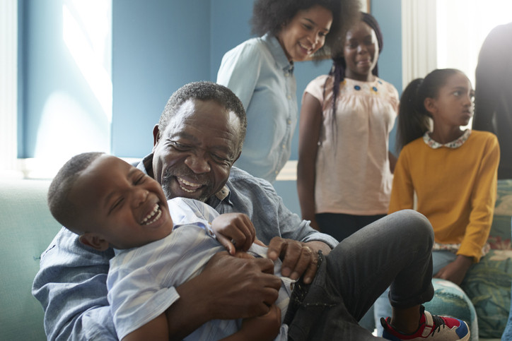 A photo of a happy senior man playing with boy while sitting on sofa at home.