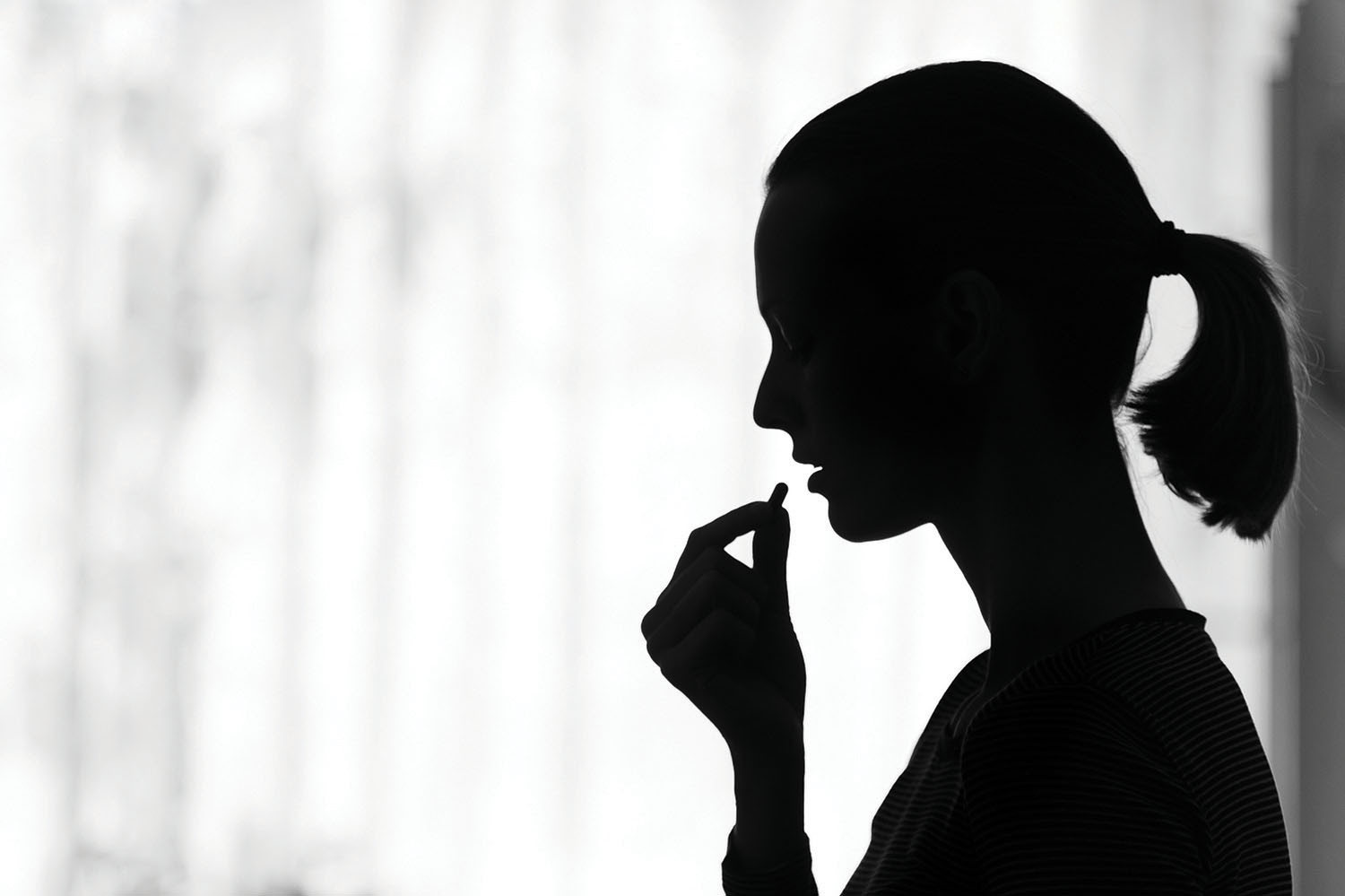 photo of a woman in silhouette holding a pill near her mouth about to take it
