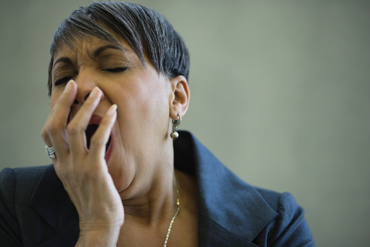 A photo of an African-American woman in her 50s yawning with her eyes closed. 