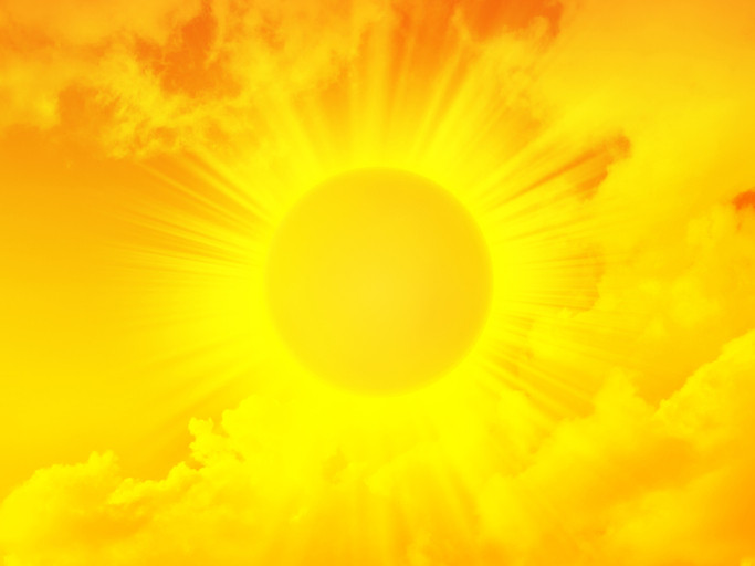 Fiery yellow sun with sun rays on a yellow-red background with clouds.The concept is heat stroke