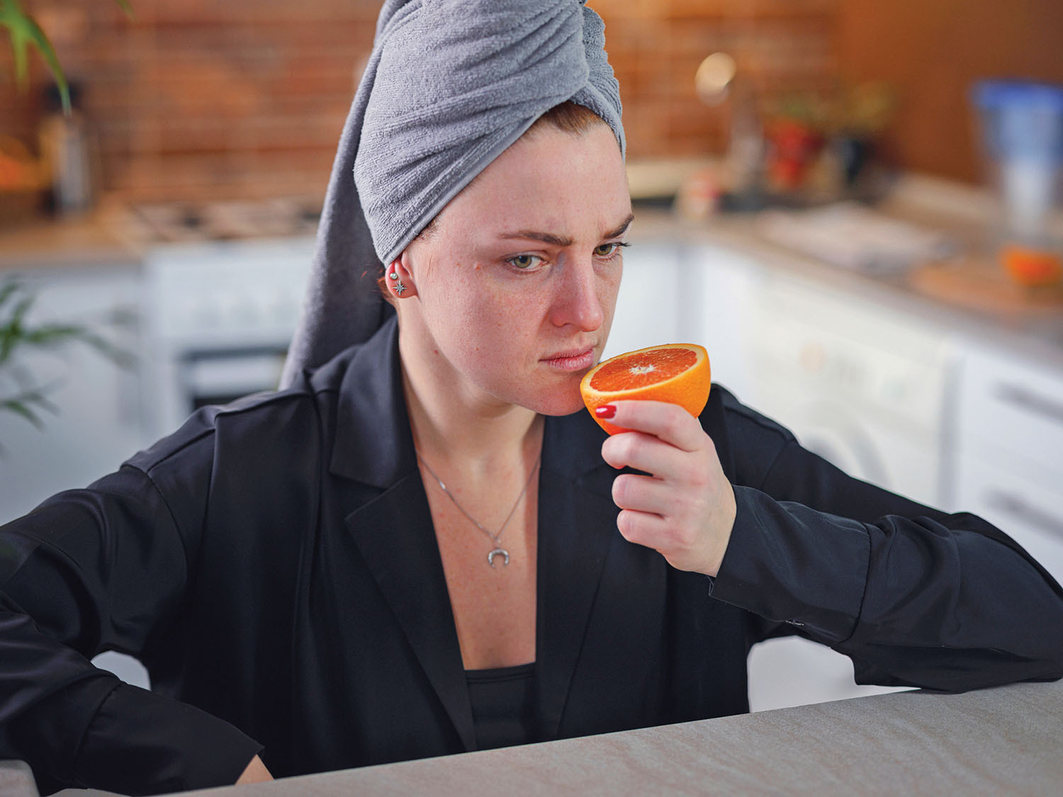 photo of a woman in her kitchen smelling a cut orange half; she has her hair wrapped in a towel