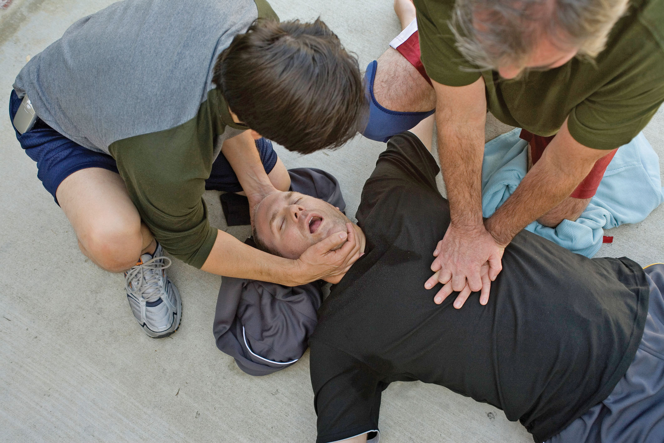 photo of a man in distress on the ground with two people performing CPR on him