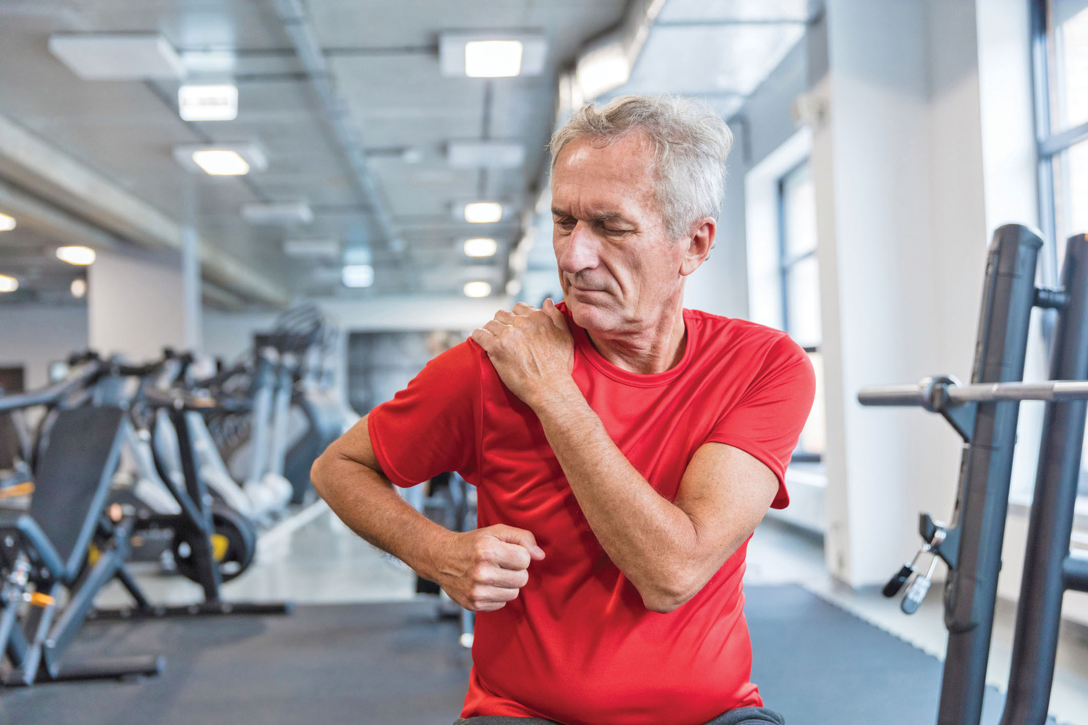 photo of a mature man in a gym rubbing his sore shoulder