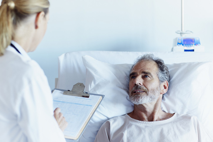 A photo of a female doctor writing notes while talking to male patient in hospital ward.