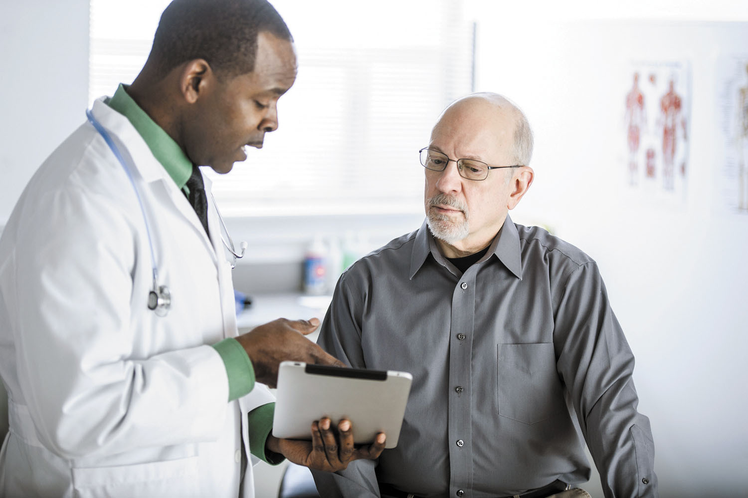 photo of a patient talking with a doctor, doctor is holding a tablet and pointing to it as they talk