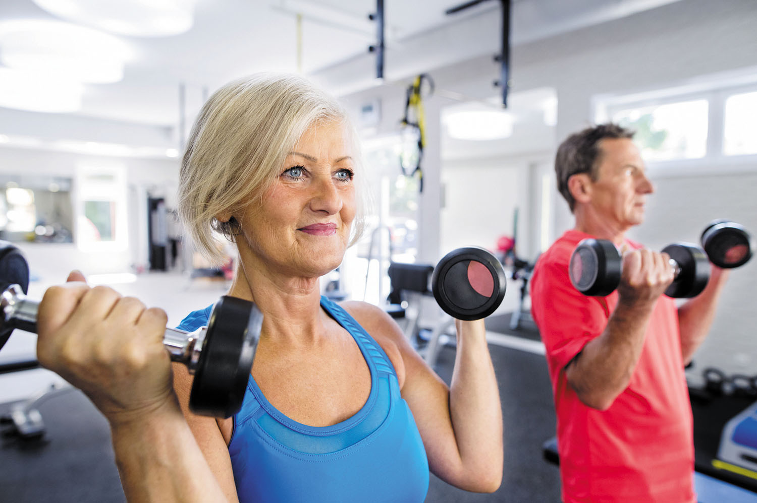 photo of a mature woman and man working out in a gym, each is doing exercises with hand weights