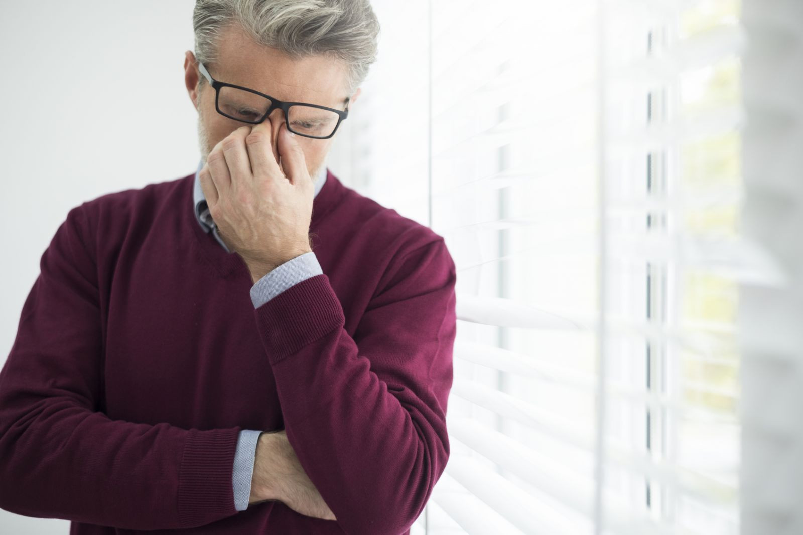 A mature man holding the bridge of his nose. 