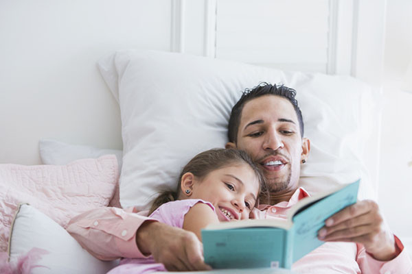 photo of a father reading to his daughter while they snuggle in bed