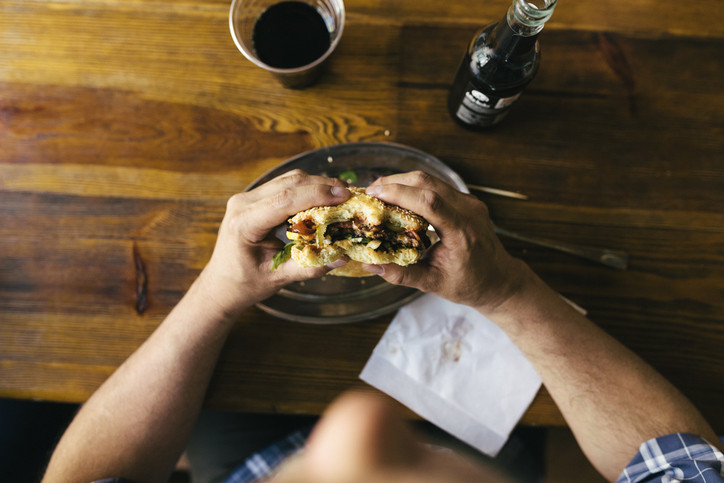 A photo of an aerial view of a man eating a burger and drinking cola in a restaurant.