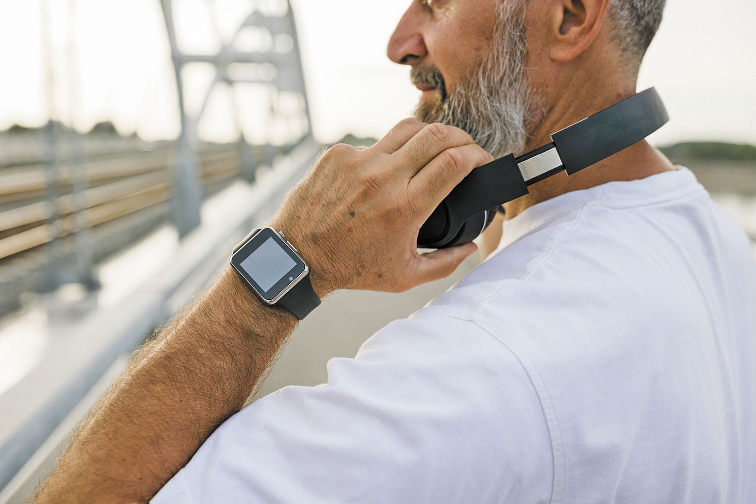 photo of a man grasping his headphones as he prepares to run outdoors; a smartwatch is visible on his left wrist