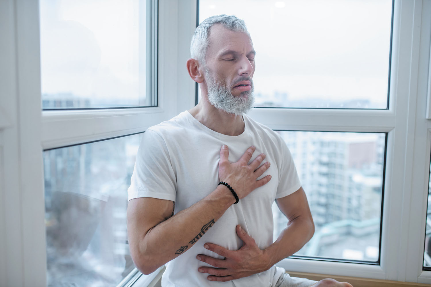 photo of a man sitting, with one hand over his heart and the other on his abdomen as he practices tactical breathing