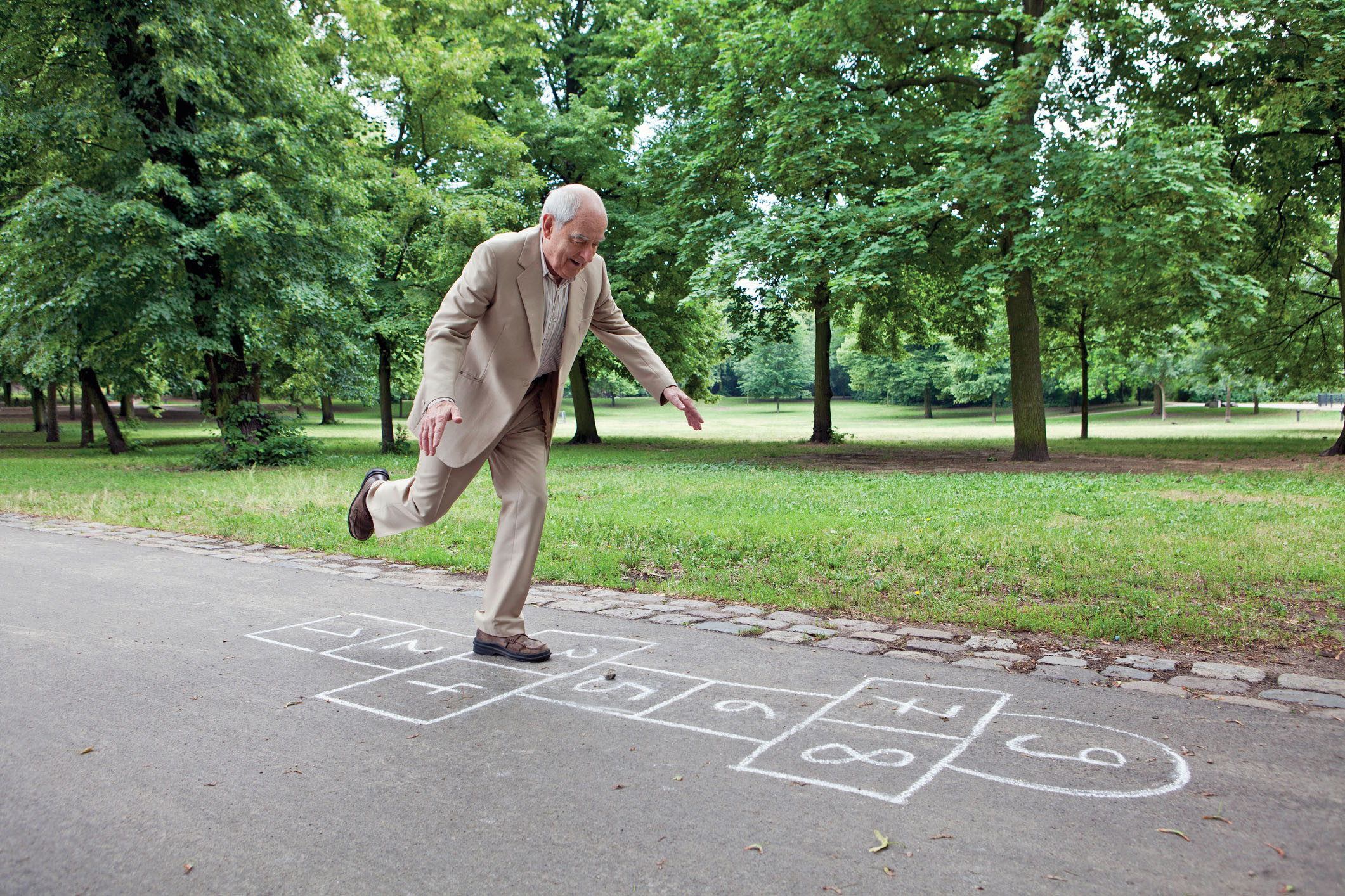 photo of an older man jumping through a game of hopscotch drawn on a sidewalk in a park