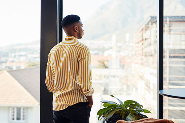 photo of a young man with his back to camera looking out a floor to ceiling window several stories above the ground