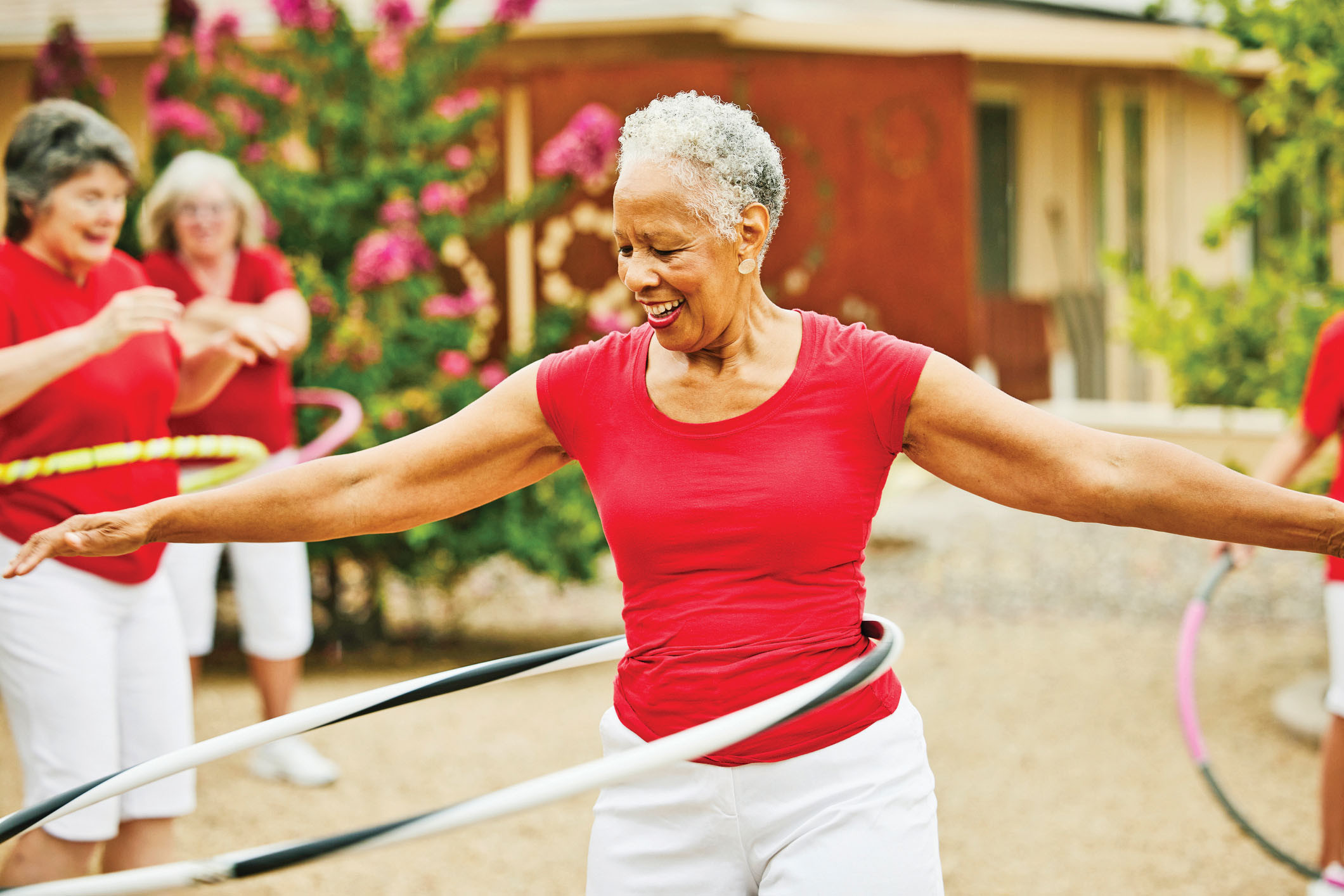 photo of a senior woman hula-hooping outdoors; two other women are visible in the background doing the same thing