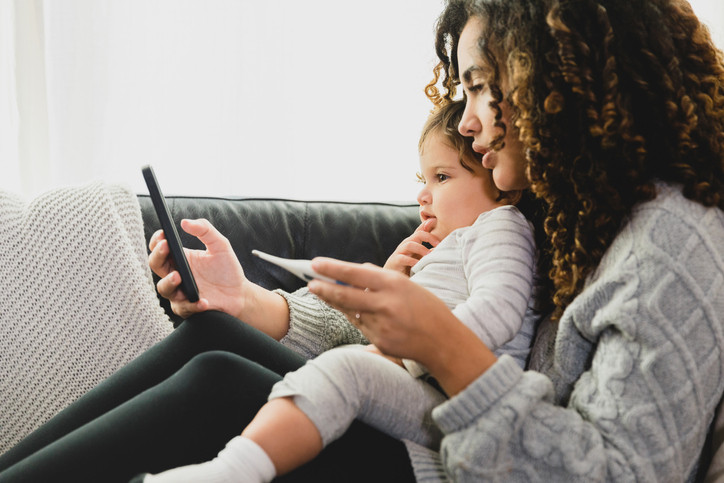 Woman holding baby and thermometer on video call with doctor