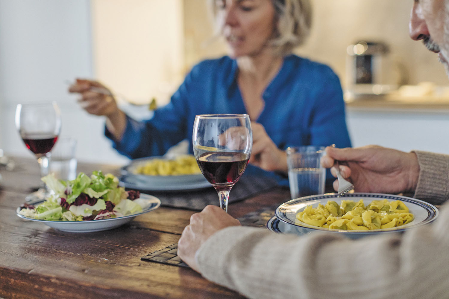 photo of a senior couple eating dinner at home with plates of food and glasses of wine on the table