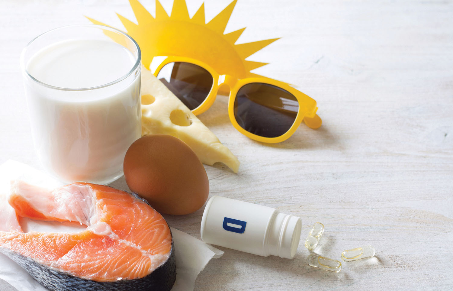 photo representing the ways people can increase vitamin D intake: diet (glass of milk, cheese, egg, salmon); sun exposure (sunglasses); bottle of supplements