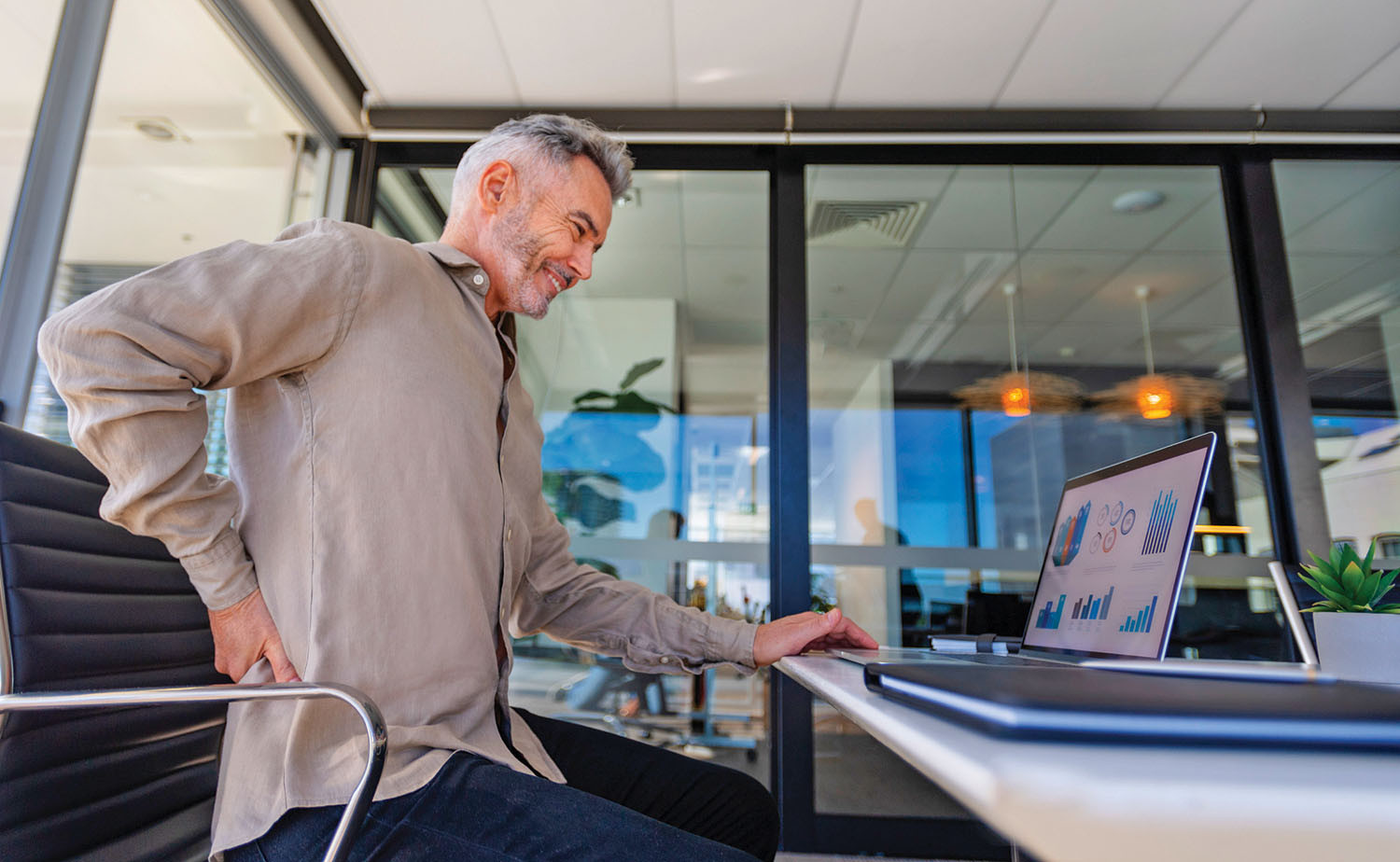 photo of a man sitting at a desk holding his hand on his lower back and grimacing in pain