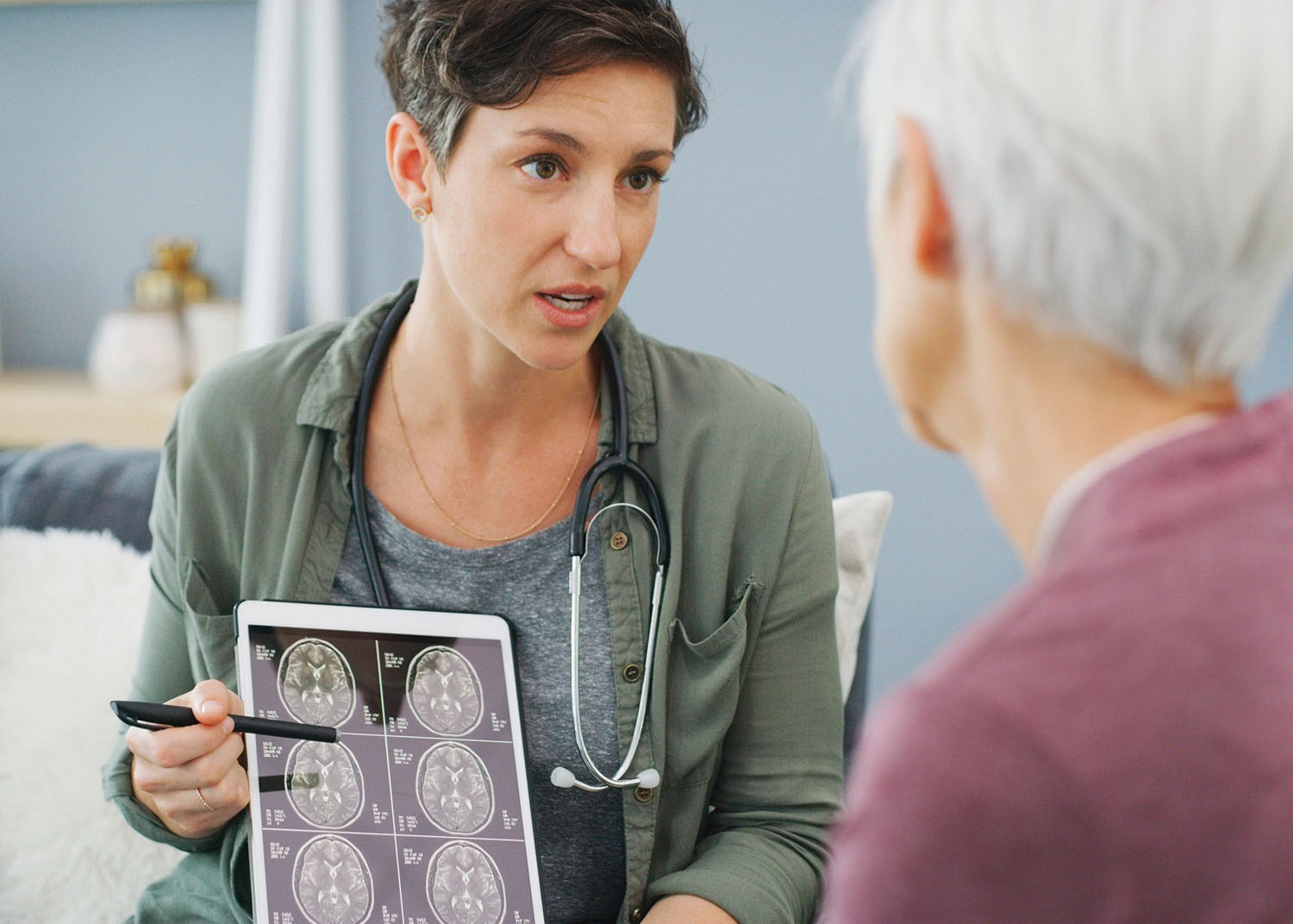 photo of a doctor talking with a patient while holding a tablet with MRI images on it