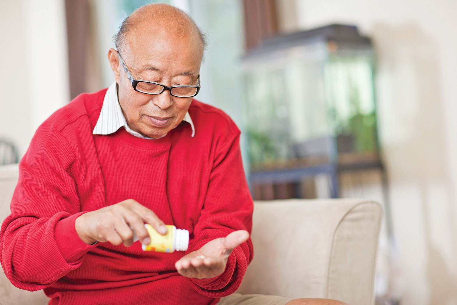 photo of an older man holding a bottle of pills and tipping one out into his hand