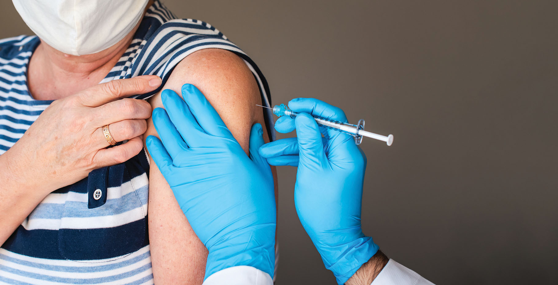 cropped photo showing the upper arm of a person receiving a vaccination and the gloved hands of the person administering it