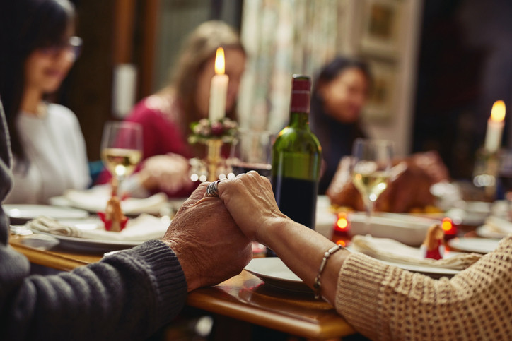 Closeup shot of people holding hands in prayer before having a meal together.