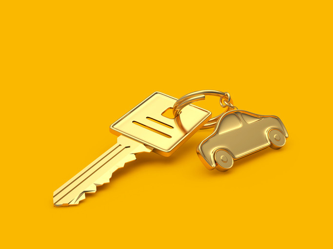 A square-topped gold car key and a gold car on a key ring against a deep yellow background