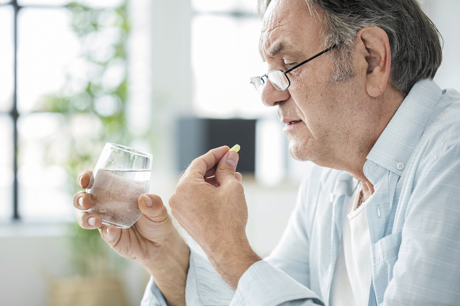 photo of a man holding a pill in his left hand and a glass of water in his right hand