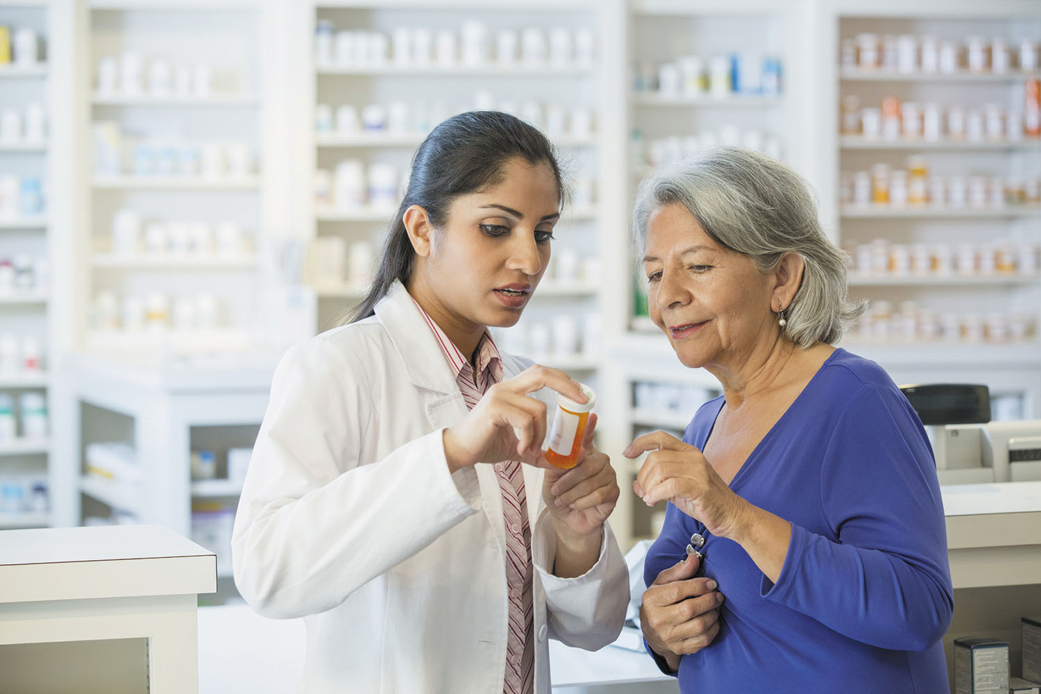photo of pharmacist discussing medication with a customer, holding the bottle in her hand and pointing to the label