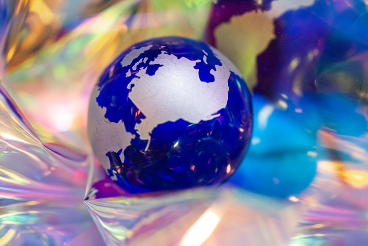 A deep blue and silver glass planet Earth in the middle of a blurred colorful, prismatic background 