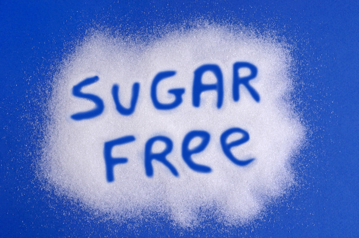 A blue background sprinkled with white sugar substitute crystals with the words sugar free written; concept is sugar alcohols and artficial sweeteners