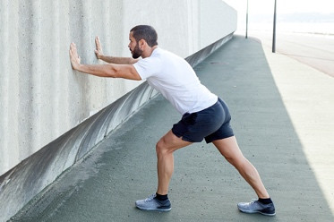 photo of a person with his palms against a wall as he performs a calf stretch exercise