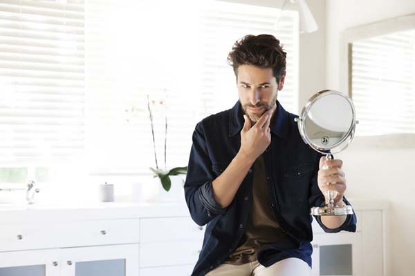 photo of a man in a bathroom admiring his reflection in a small handheld mirror
