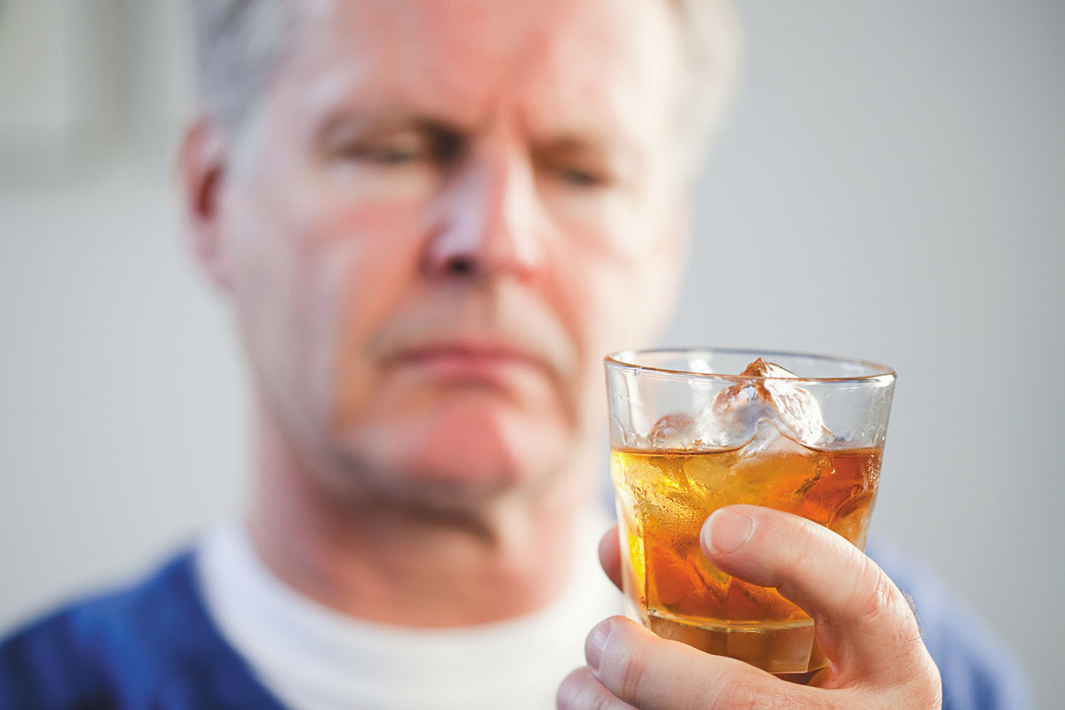 photo of a man holding a glass of liquor and looking at it skeptically