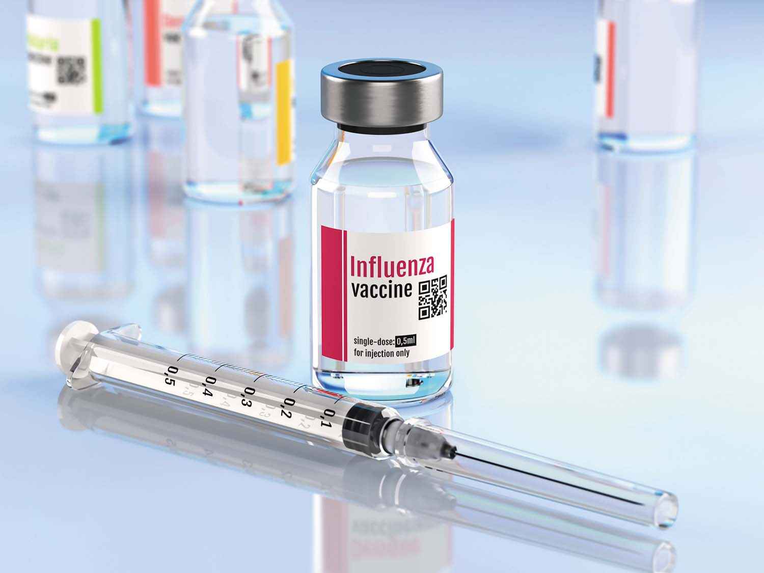 photo of a vial of influenza vaccine with a syringe laid alongside it on a reflective counter surface