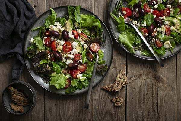 photo from above of two plates filled with salad containing bright green lettuce, grape tomatoes, feta cheese, kalamata olives, and slices of avocado