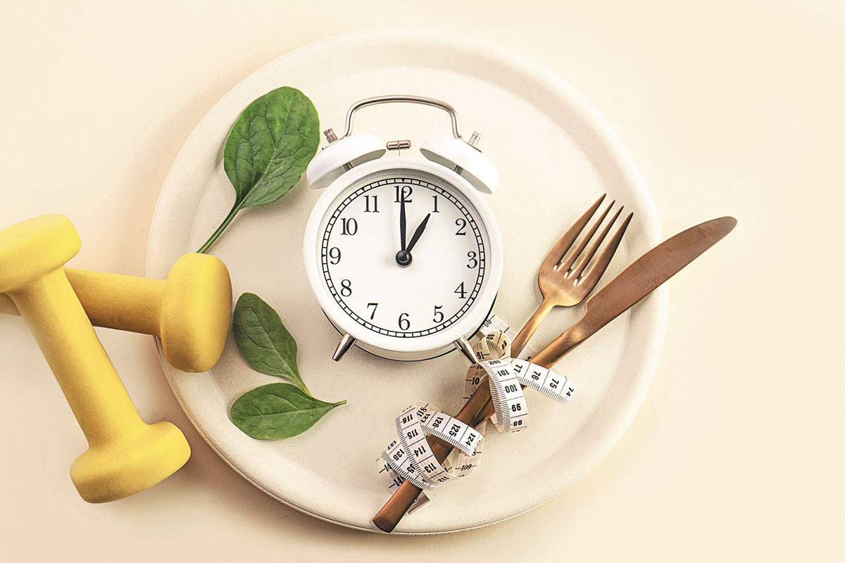 photo of an alarm clock on a dinner plate with a measuring tape entwined around a fork and knife and hand weights on the side