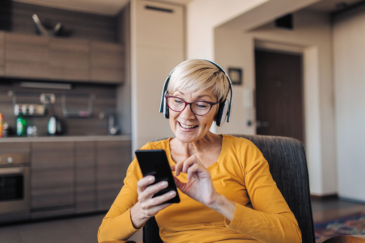 photo of a woman in her home using her smartphone while wearing headphones