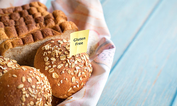 close-up photo of a basket holding rolls and sliced bread, with a small yellow sign reading gluten-free on a toothpick stuck into one of the rolls