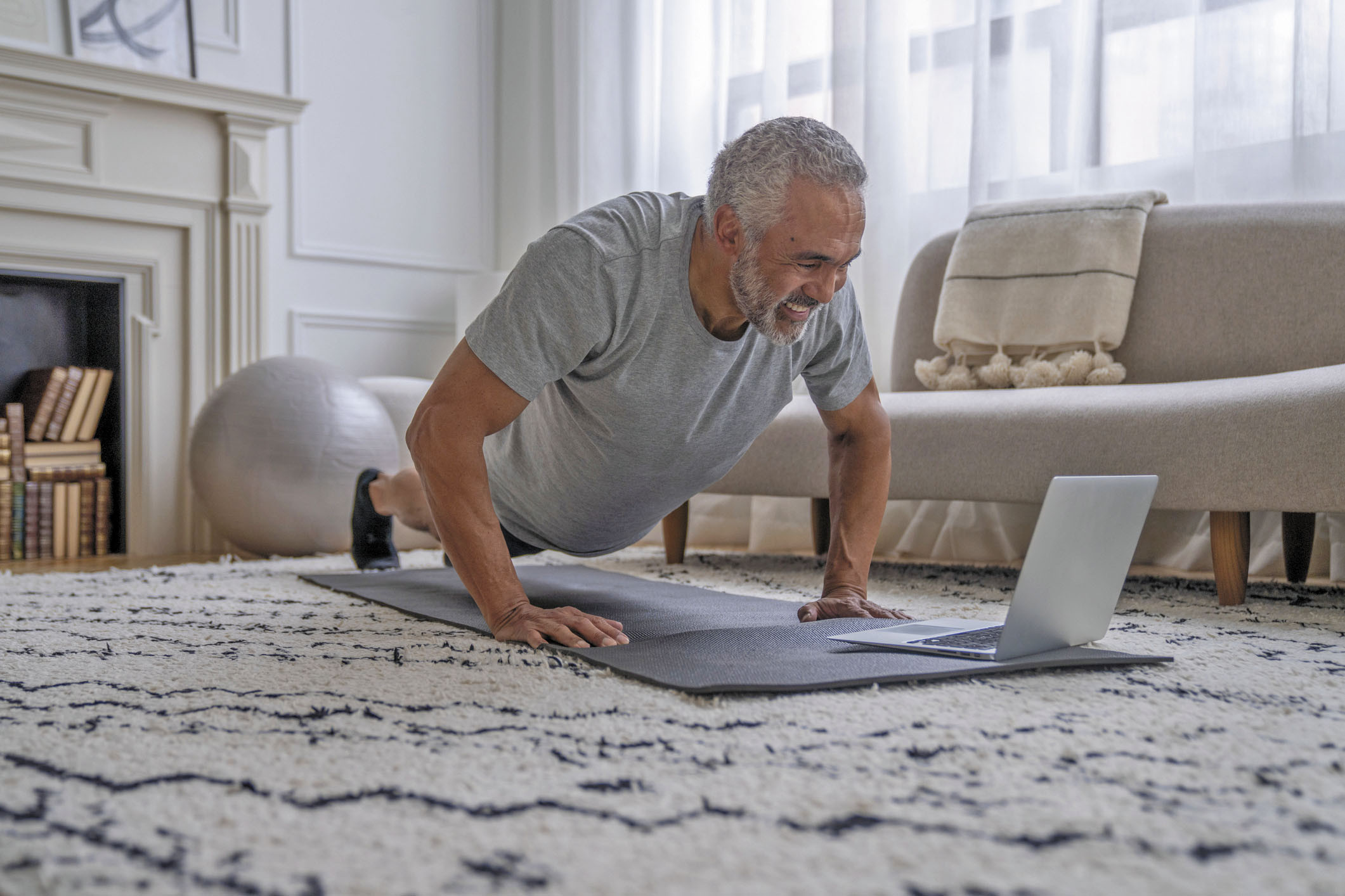 photo of a senior man doing pushups at home while using a laptop to watch an online exercise class