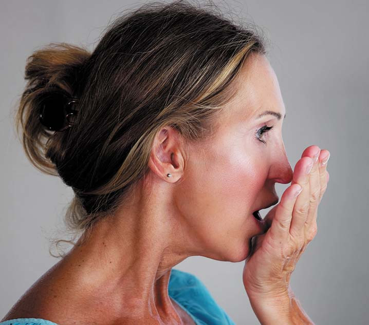 photo of a woman holding her hand in front of her mouth and blowing into the hand to check her breath