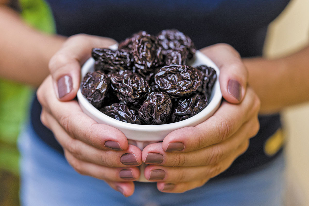 cropped photo of a woman's hands holding a bowl of prunes