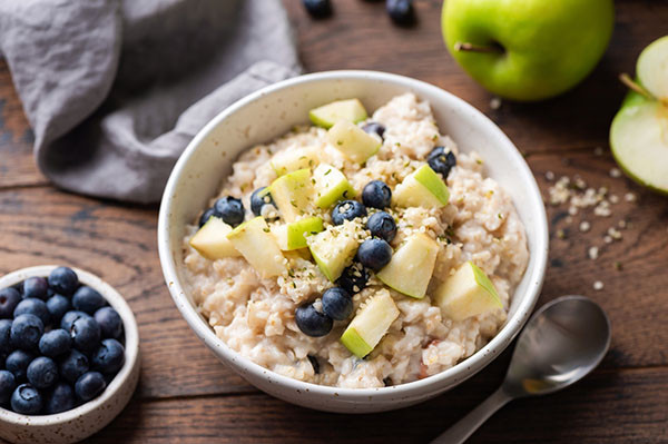 photo of a bowl of oatmeal with blueberries and chunks of green apple; a small bowl of berries and an apple cut in half are next to the bowl
