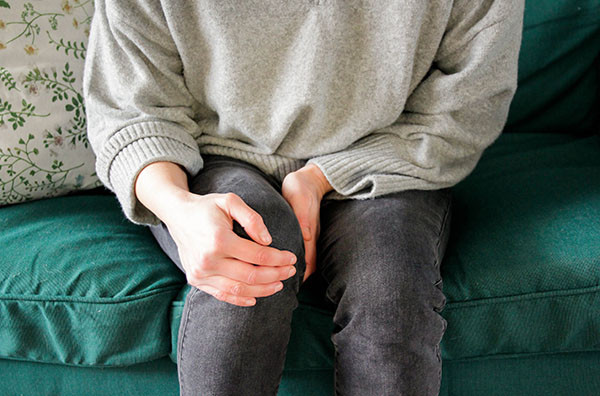 cropped photo showing a person from chest to knees, holding one knee with both hands due to pain