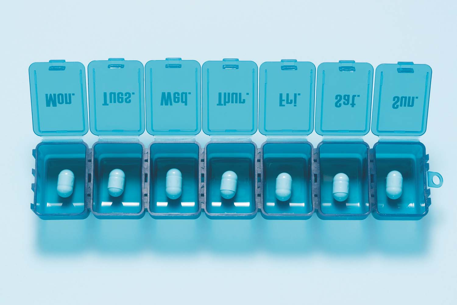 photo of a pill container with individual compartments for each day of the week, with lids open and a single pill in each compartment