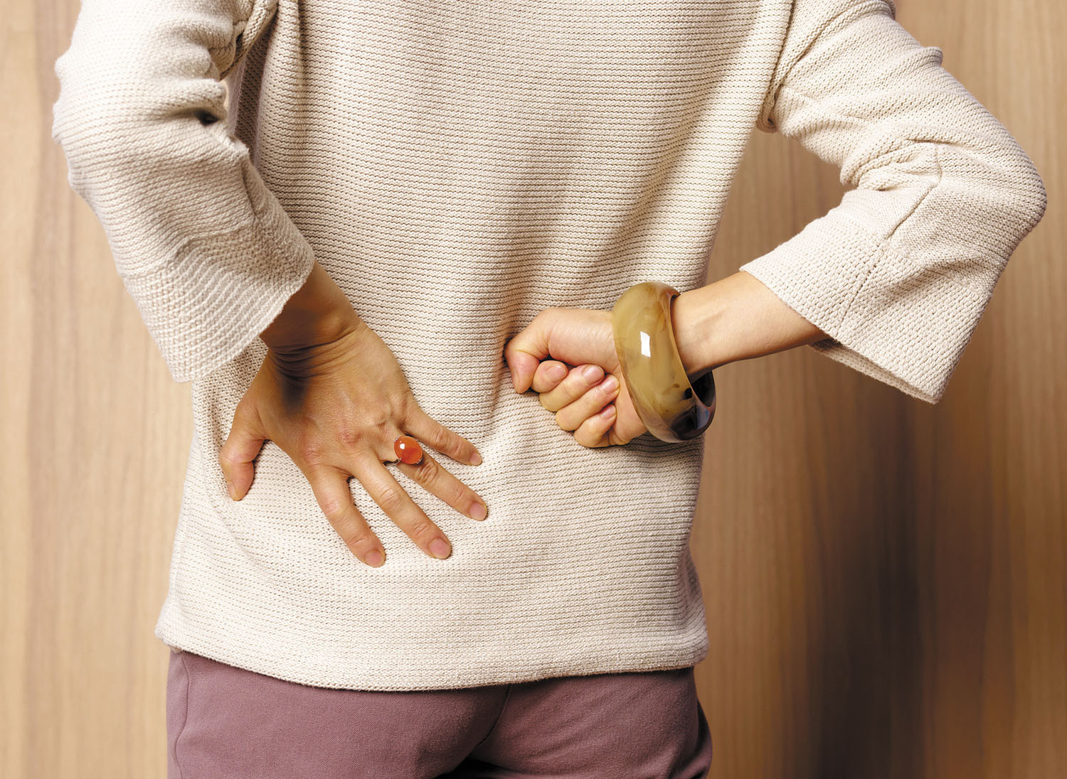 photo of a woman viewed from behind holding her hands on her back due to pain from kidney stones