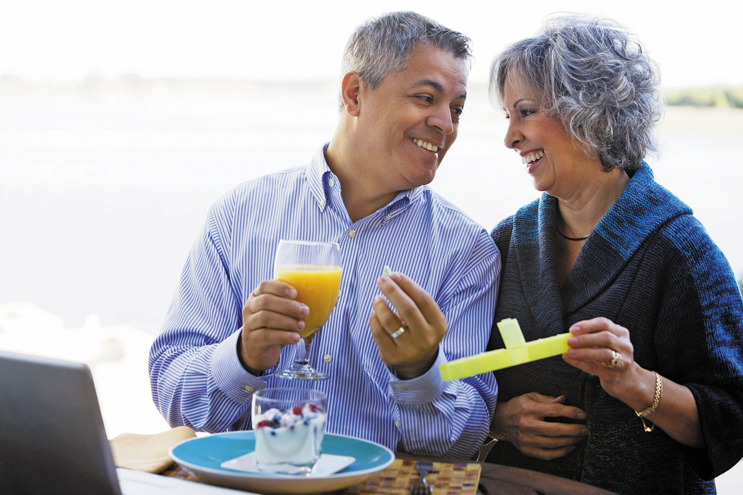 photo of a mature couple taking their medications as they enjoy breakfast outdoors