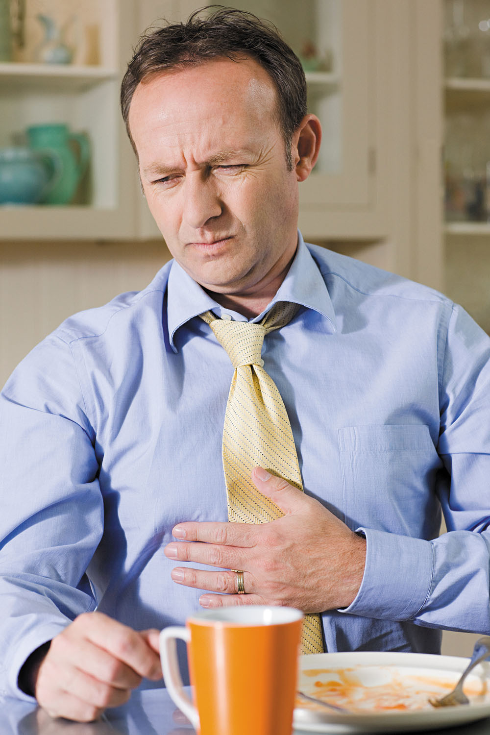 photo of a man experiencing stomach discomfort, holding his hand to his abdomen and wincing
