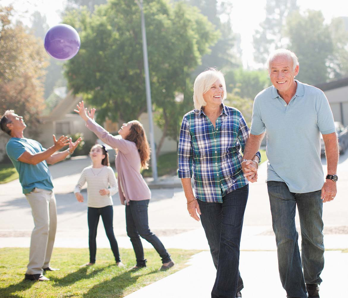 photo of a senior couple walking outdoors; a father, mother, and child are seen playing with a large ball in the background