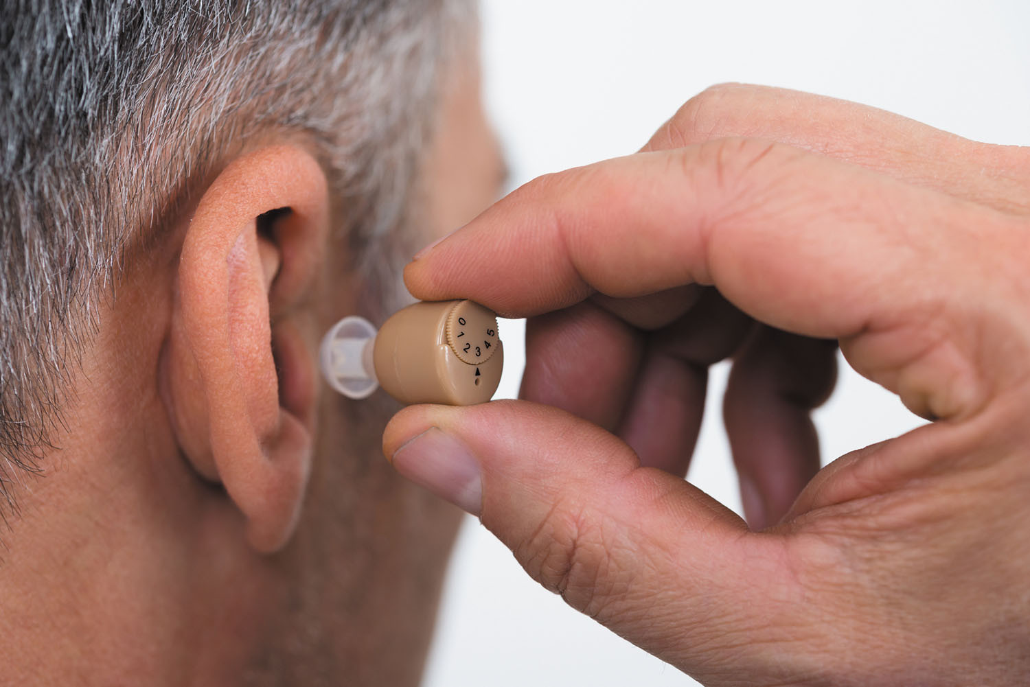 close-up photo of a man's head viewed from behind, he is inserting a hearing aid into his right ear